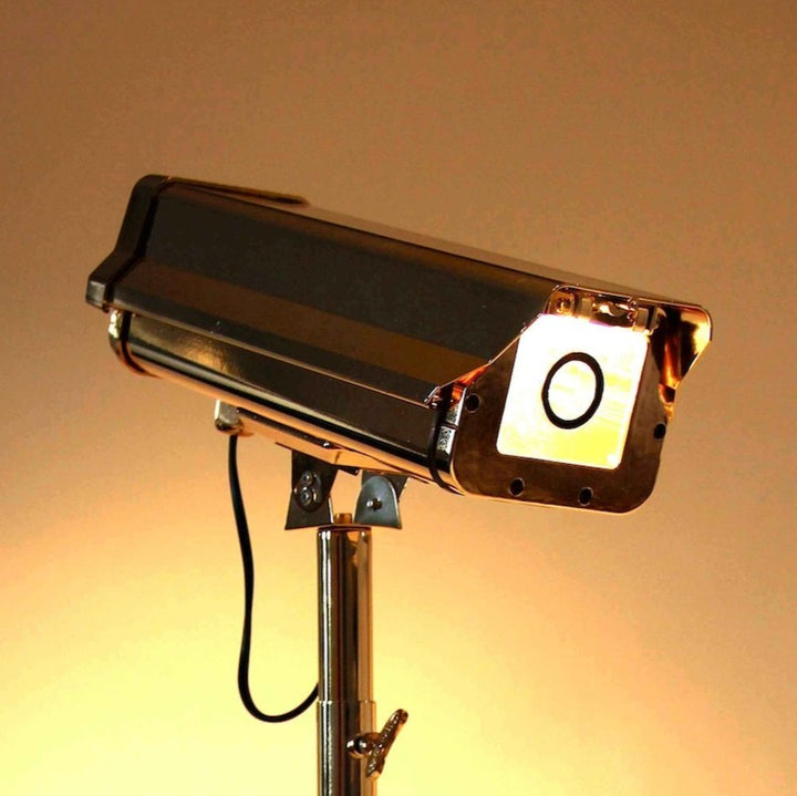 “CCTV Lights – Desk Top” by Ben Rousseau – a sculptural gold-plated LED lamp on a tripod base, reimagining the CCTV camera as a symbol of modern luxury and design. A provocative fusion of technology, art, and illumination.
