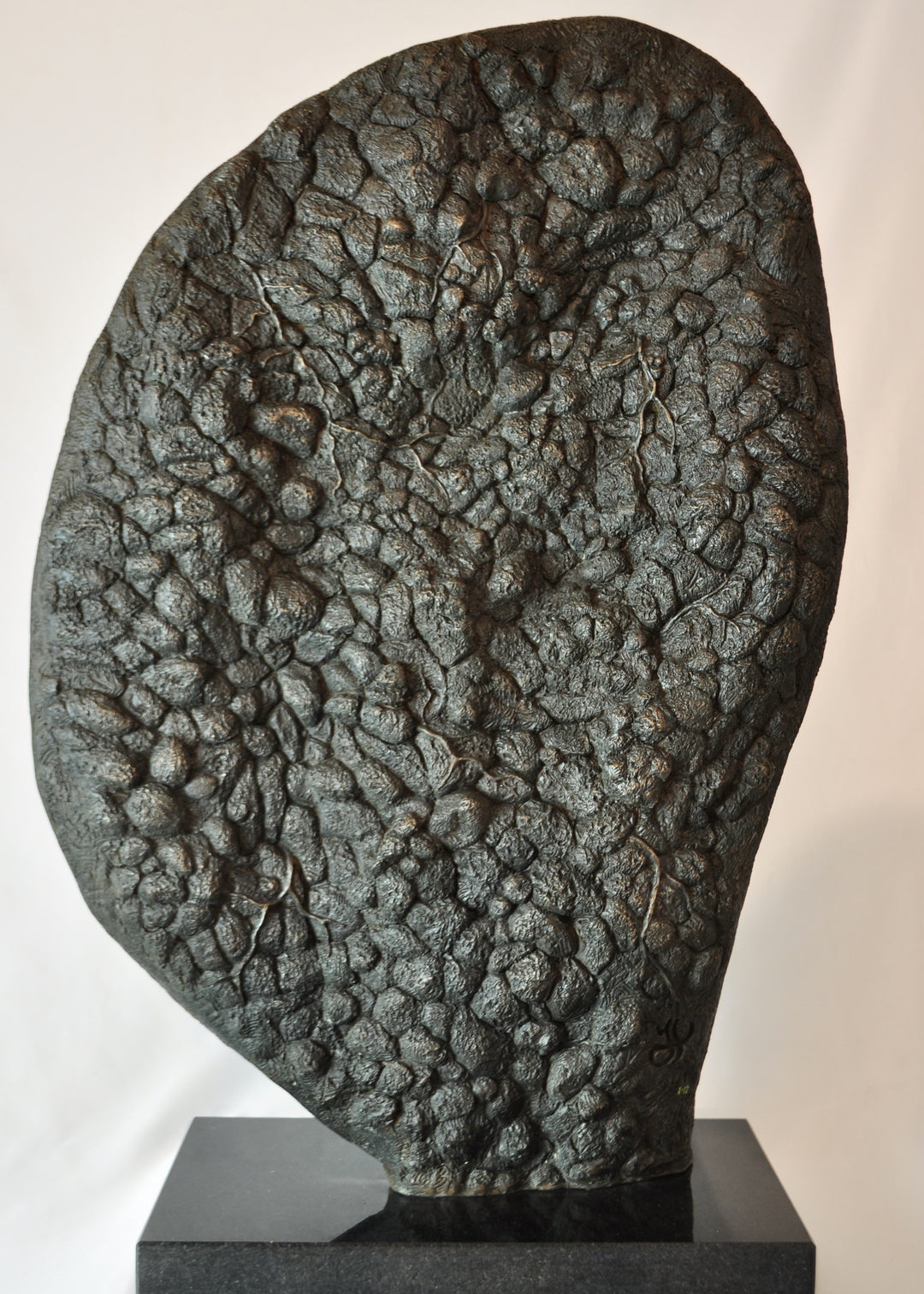 A hand-painted bronze bas-relief sculpture depicting a reclining female form emerging from dense spring foliage, with leaves, ferns and flowers flowing across her body, blending seamlessly into textured earth around the edge.