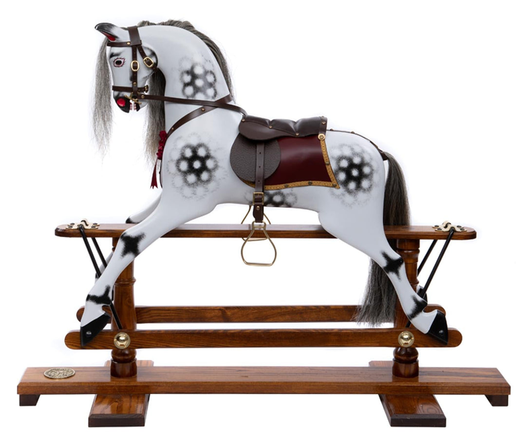 White rocking horse with stylised black dapples, grey mane, and rich burgundy leather tack on a polished oak safety stand.

