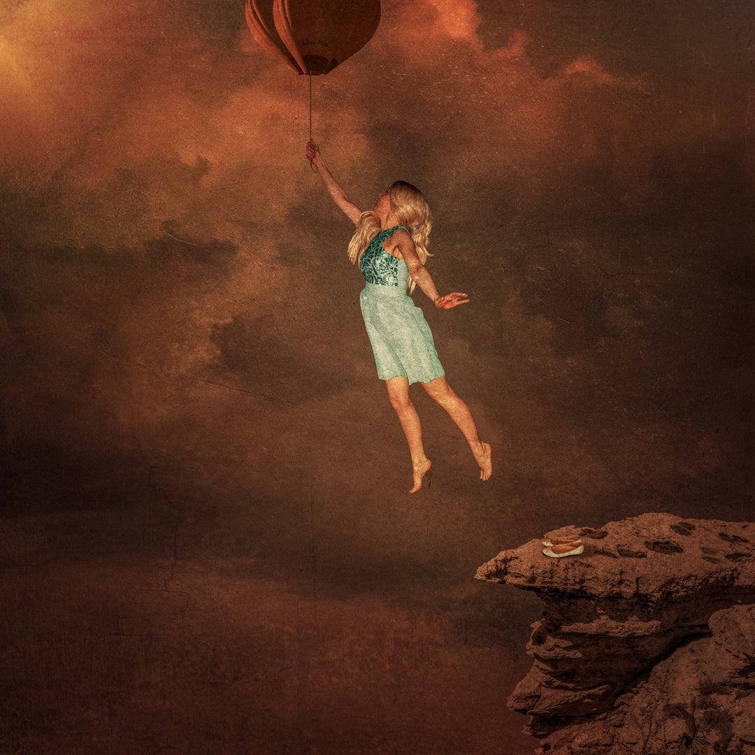 A blonde woman in a teal dress floats mid-air, clutching the string of a small, whimsical balloon above a dramatic canyon edge. Her bare feet dangle as she rises away from a rocky ledge, where a vintage flying helmet and goggles rest, suggesting flight, risk, and imagination. The moody, textured sky glows in tones of rust and gold, adding tension and surreal drama to the scene.