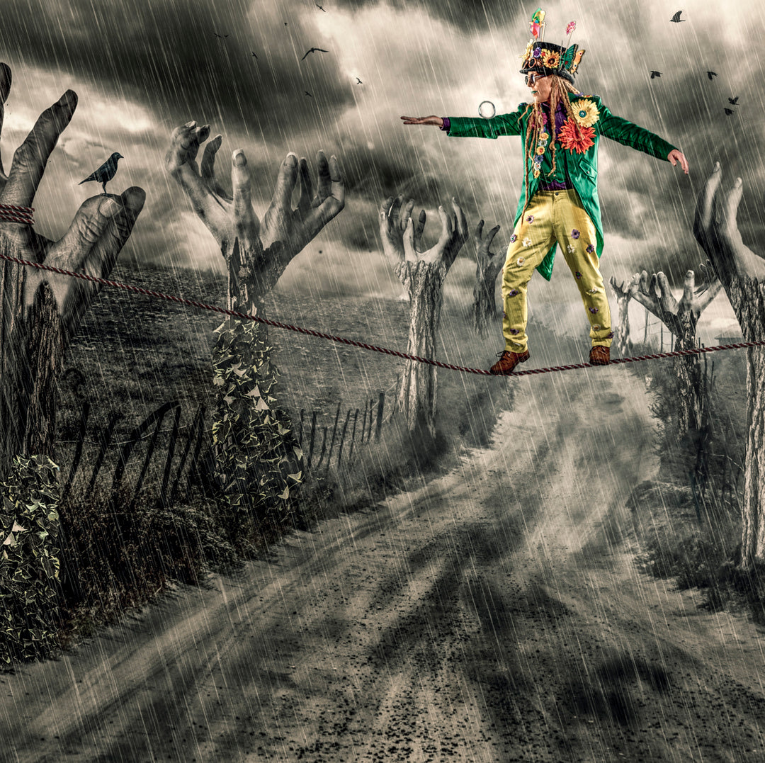 A surreal image of a colourfully dressed man walking a tightrope in heavy rain, balancing above a desolate path lined with eerie, tree-like hands reaching from the ground. Dark clouds swirl above as crows and birds fly through the stormy sky. The figure wears a green coat, yellow trousers, and a whimsical hat adorned with flowers and accessories, symbolising resilience and eccentricity in the face of chaos.