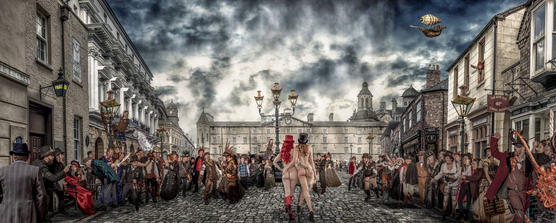 A panoramic, digitally constructed fantasy scene featuring a cobbled street filled with elaborately dressed Victorian steampunk characters reacting to two nude women in red and black top hats walking confidently through the centre. The backdrop includes dramatic clouds, grand architecture, and surreal details like a flying airship and exaggerated facial expressions, creating a vivid tableau of spectacle and rebellion.