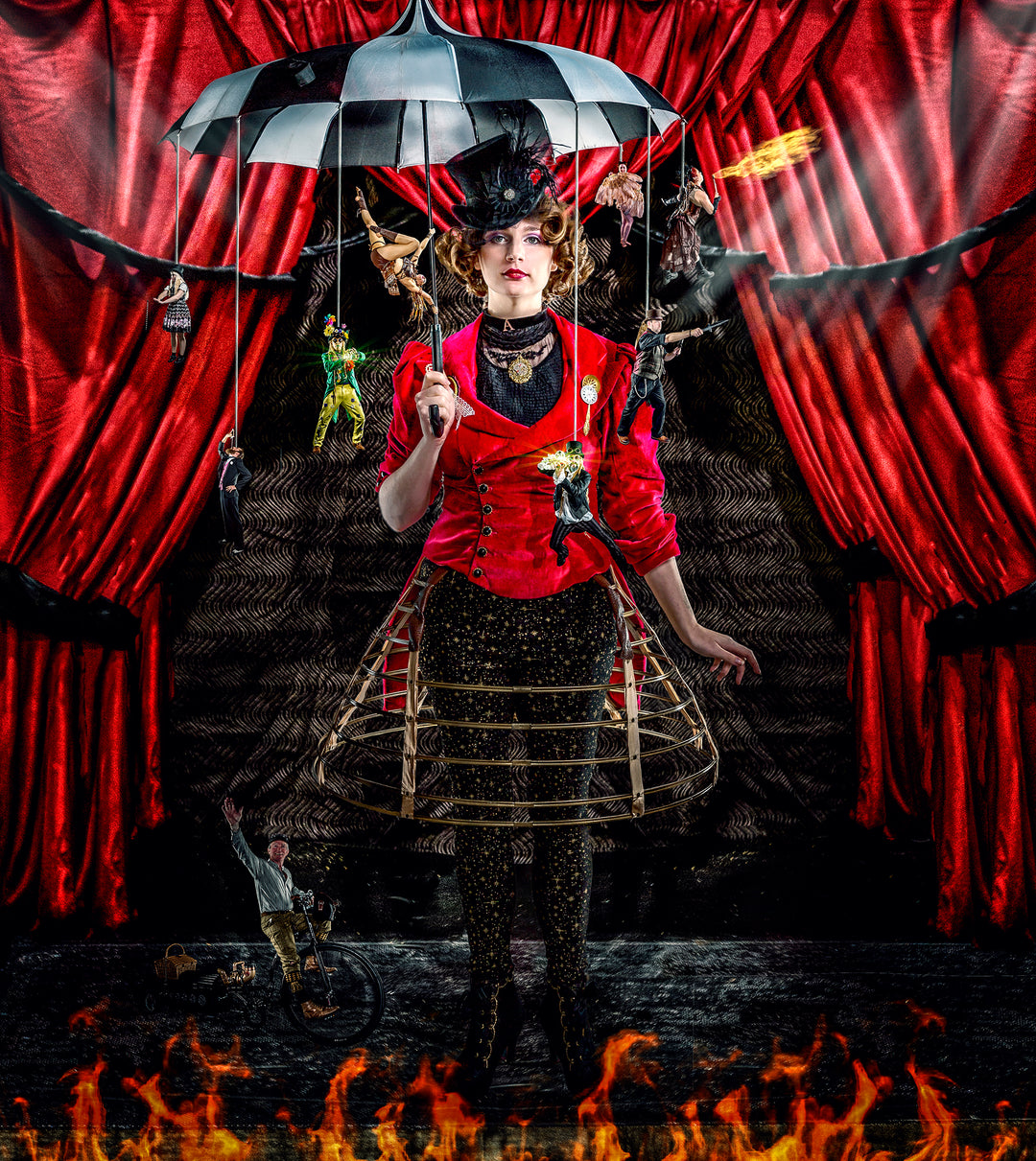A theatrical woman in a red velvet jacket and top hat stands centre stage beneath an umbrella, from which miniature circus performers dangle like marionettes. Behind her, dramatic red curtains frame a surreal scene of fire, acrobatics, and fantasy in a rich, steampunk-inspired setting.
