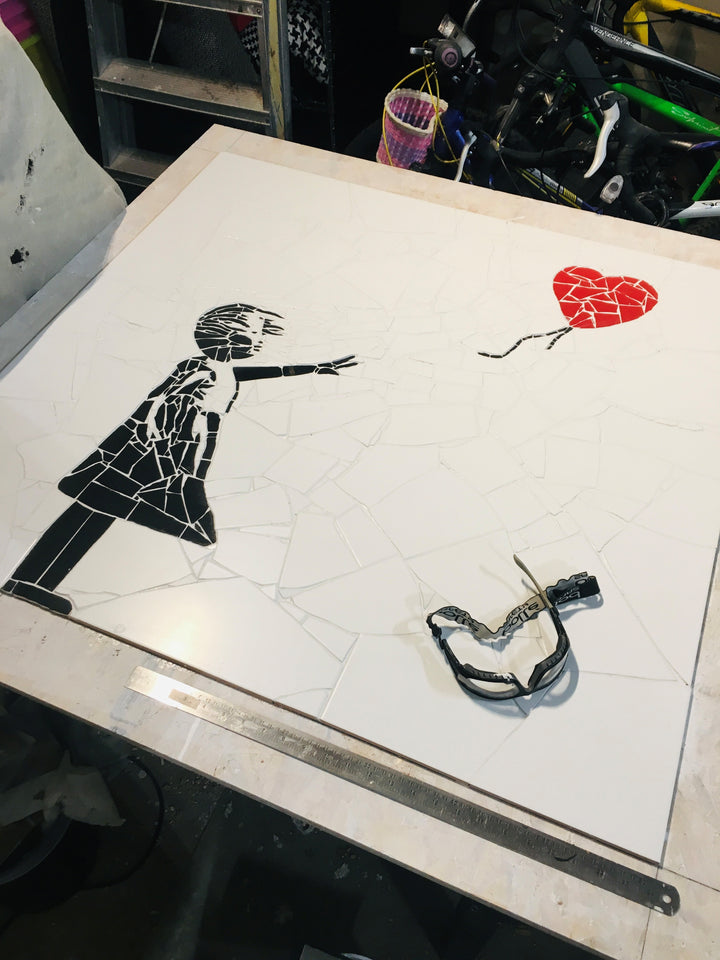 “Girl with Balloon” mosaic — a handcrafted ceramic tile artwork reimagining the iconic heart balloon image. Featuring black and white tiles with a vivid red heart, this bespoke commission blends street art symbolism with fine mosaic craftsmanship.