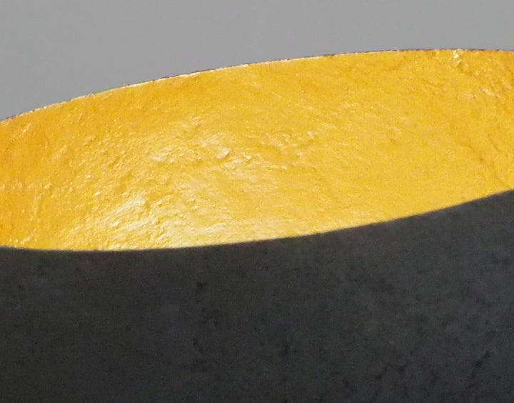 Glow: 22ct Gold by Tracy Nicholls — a one-off kiln-cast glass vessel made using the pâte de verre technique. The piece features a thin, eggshell-like black glass exterior with a rough, volcanic texture, contrasted by a luminous interior lined with 22ct gold leaf. Light reflects across the curved golden surface, creating the illusion of an inner radiance, as though the vessel itself glows from within.
