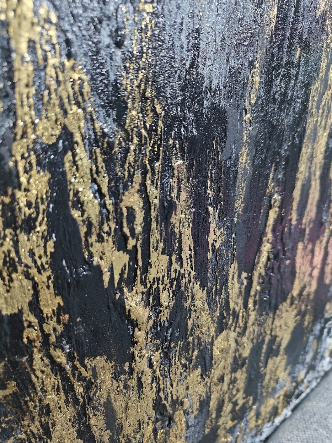 Textured abstract painting with vertical strokes in gold, black, and grey tones on a rough, layered surface