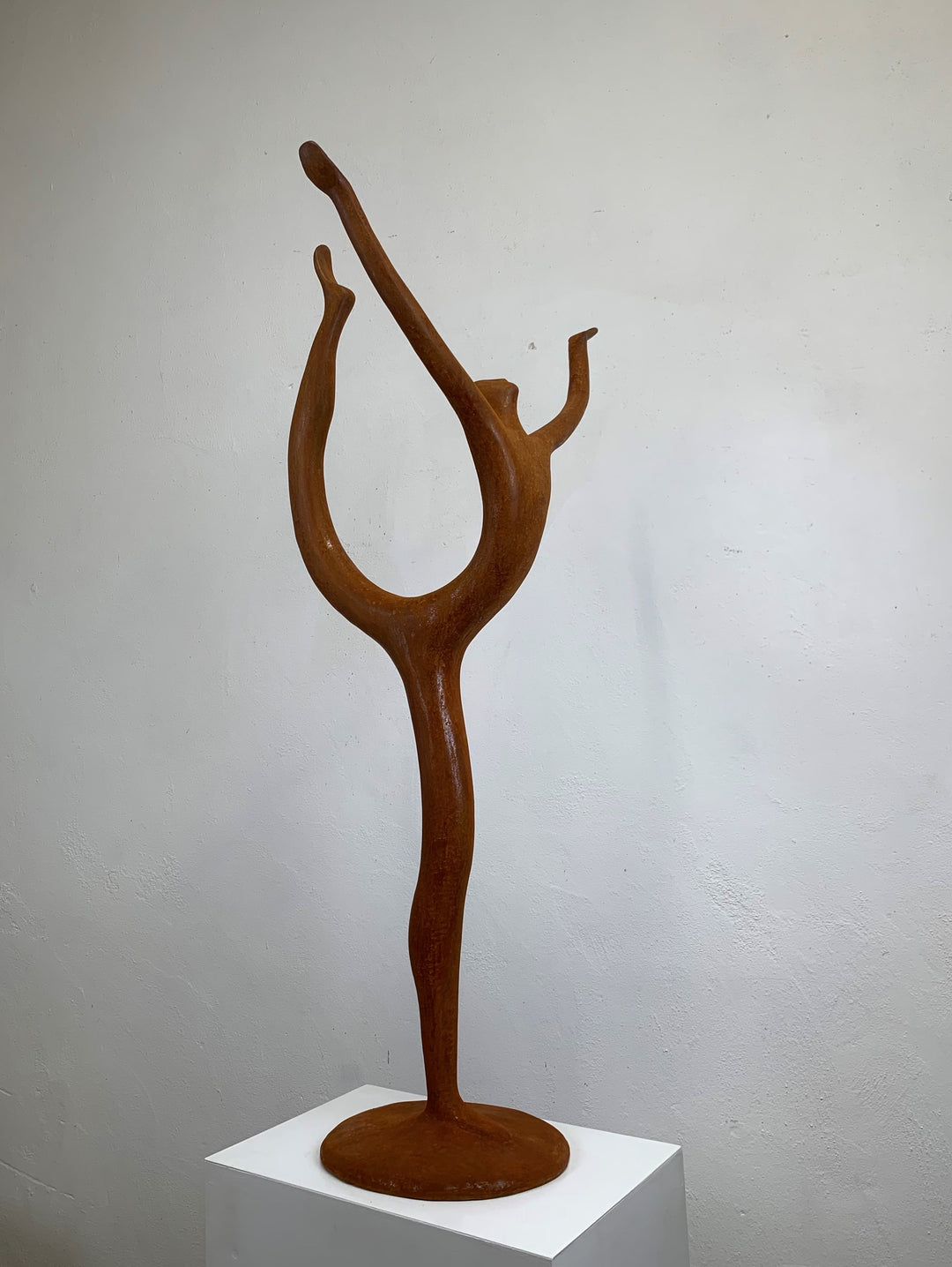 Rust-coloured bronze sculpture of an abstract dancer with elongated limbs, captured mid-pose in an energetic, gravity-defying stretch.