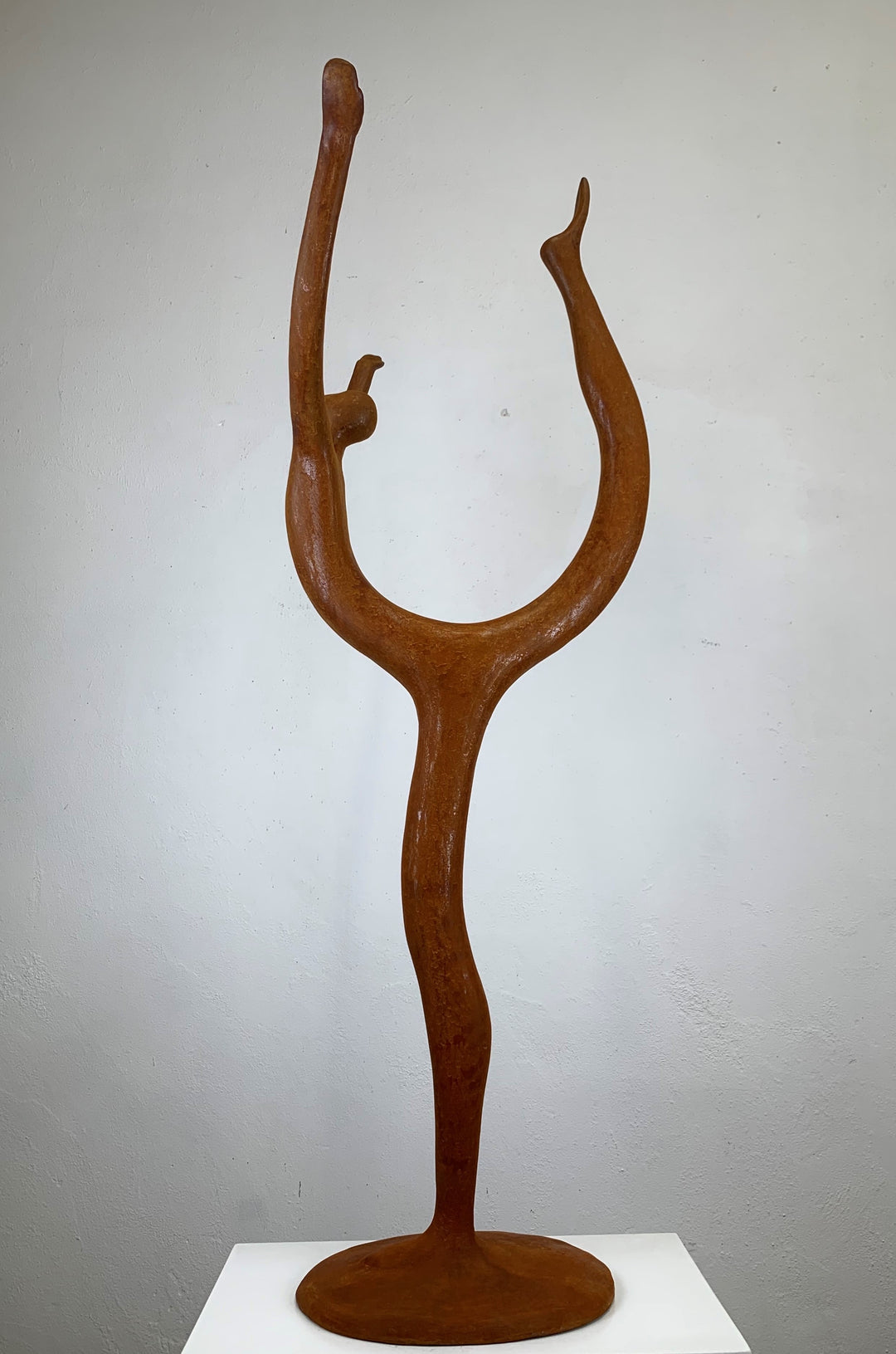 Rust-coloured bronze sculpture of an abstract dancer with elongated limbs, captured mid-pose in an energetic, gravity-defying stretch.