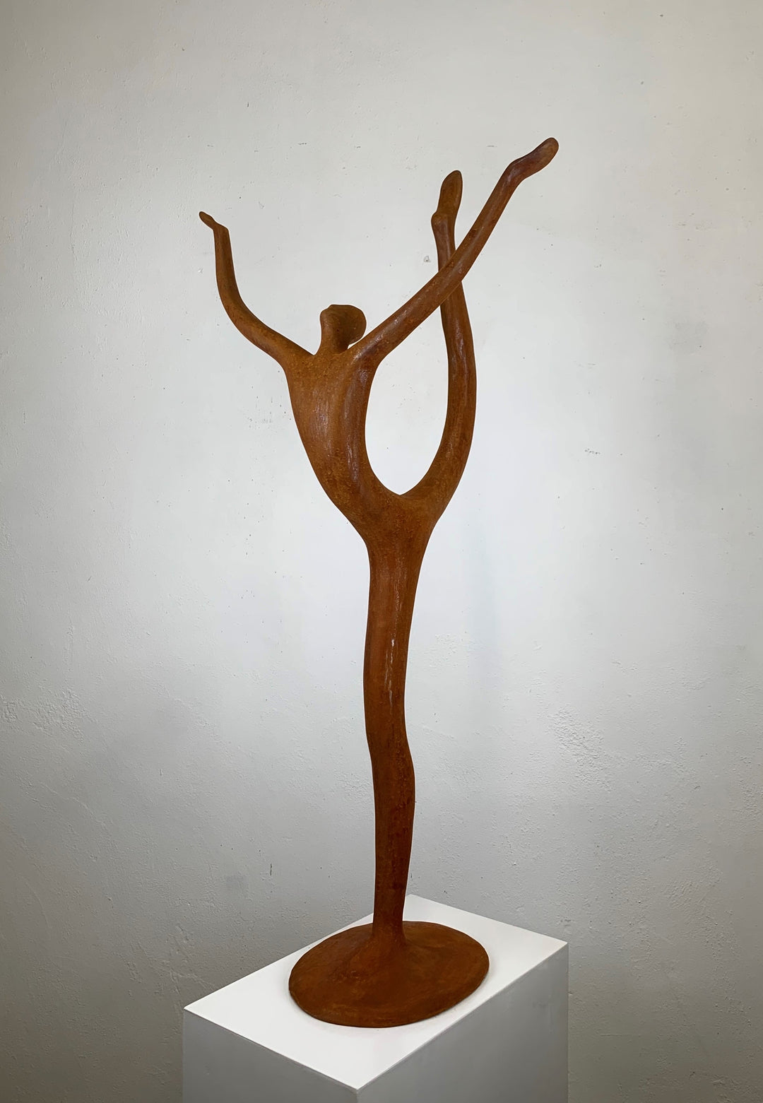 Rust-coloured bronze sculpture of an abstract dancer with elongated limbs, captured mid-pose in an energetic, gravity-defying stretch.