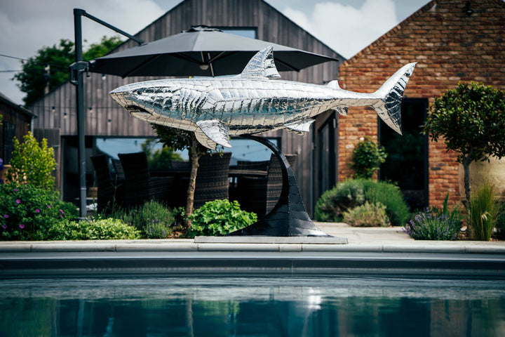 ‘Great White’ by Michael Turner, a unique, one-of-one stainless steel marine wildlife sculpture depicting a powerful great white shark swimming with its mouth partially open, exposing rows of sharp triangular teeth. Handcrafted from intricately shaped and welded stainless steel, the sculpture features a polished silver finish, detailed metallic skin, distinctive dorsal and pectoral fins and a sweeping tail. Mounted on a curved black metal support with a rectangular base, this large-scale contemporary sculpt
