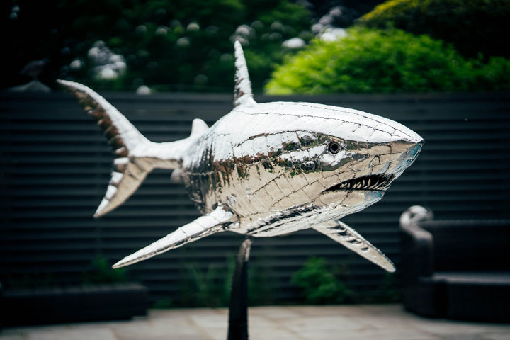 ‘Great White’ by Michael Turner, a unique, one-of-one stainless steel marine wildlife sculpture depicting a powerful great white shark swimming with its mouth partially open, exposing rows of sharp triangular teeth. Handcrafted from intricately shaped and welded stainless steel, the sculpture features a polished silver finish, detailed metallic skin, distinctive dorsal and pectoral fins and a sweeping tail. Mounted on a curved black metal support with a rectangular base, this large-scale contemporary sculpt