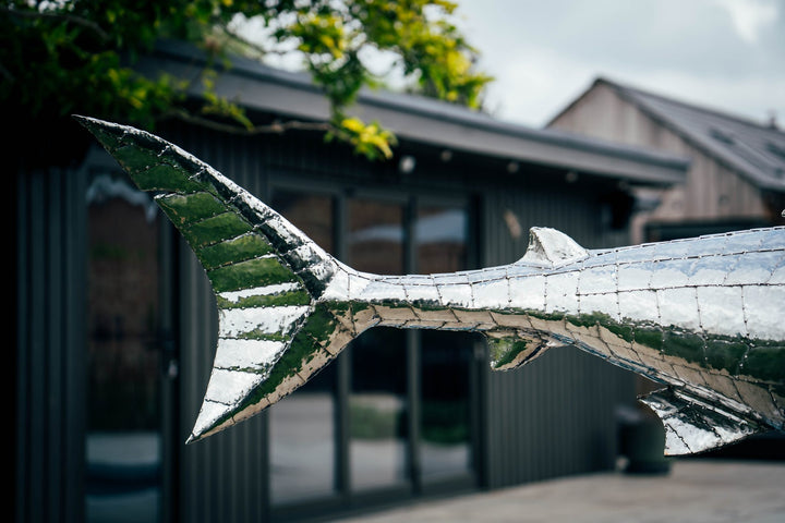 ‘Great White’ by Michael Turner, a unique, one-of-one stainless steel marine wildlife sculpture depicting a powerful great white shark swimming with its mouth partially open, exposing rows of sharp triangular teeth. Handcrafted from intricately shaped and welded stainless steel, the sculpture features a polished silver finish, detailed metallic skin, distinctive dorsal and pectoral fins and a sweeping tail. Mounted on a curved black metal support with a rectangular base, this large-scale contemporary sculpt