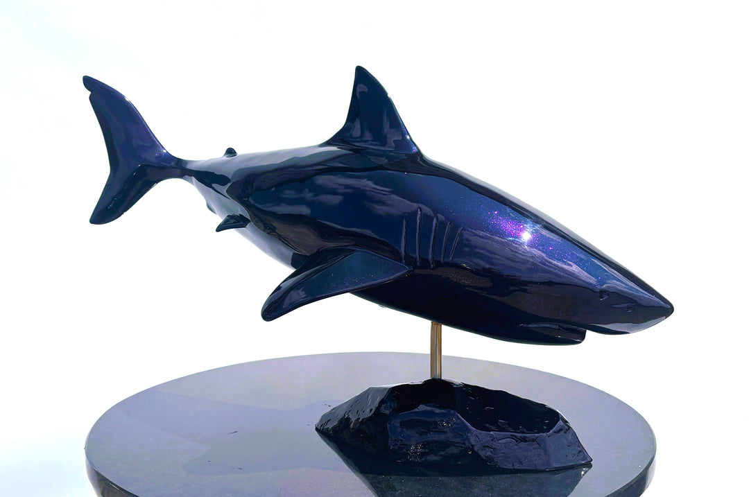 Sculpture titled Great White IV.2 (2025), depicting a stylised great white shark cast in deep blue Jesmonite with a high-gloss finish, mounted on a dark rock-like base.