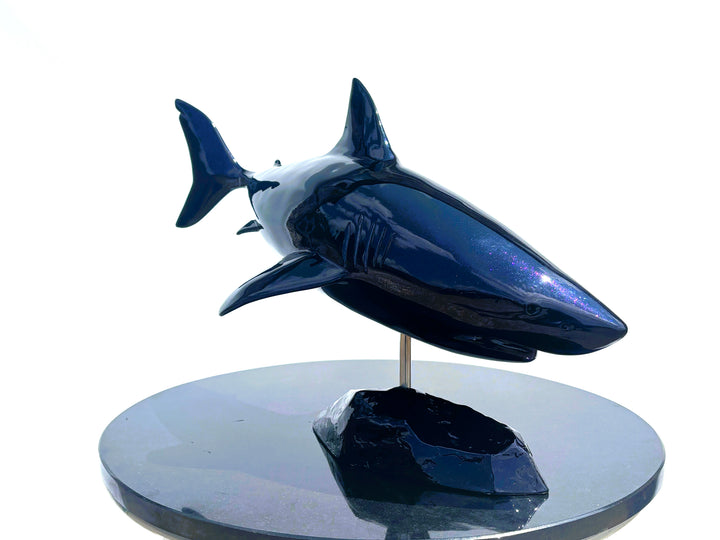Sculpture titled Great White IV.2 (2025), depicting a stylised great white shark cast in deep blue Jesmonite with a high-gloss finish, mounted on a dark rock-like base.