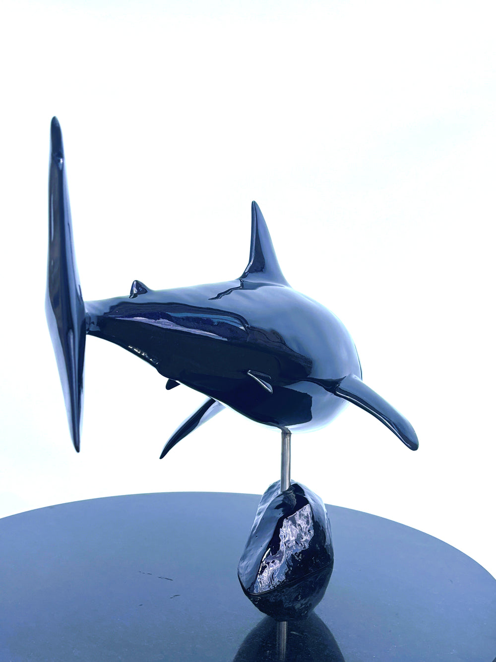 Sculpture titled Great White IV.2 (2025), depicting a stylised great white shark cast in deep blue Jesmonite with a high-gloss finish, mounted on a dark rock-like base.