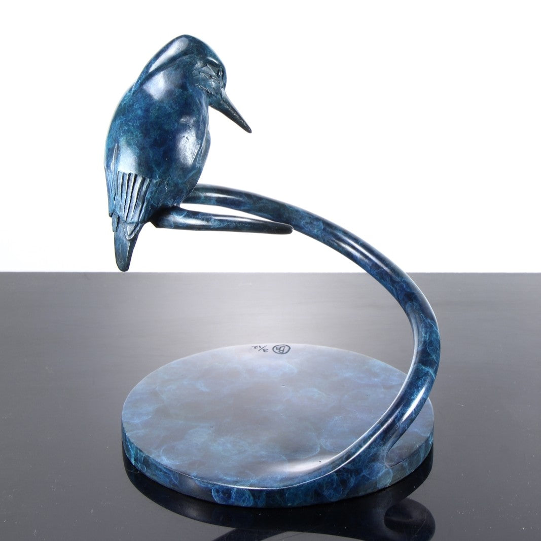 ‘Halcyon Days Maquette’ by Pat Bull, a limited-edition contemporary bronze wildlife sculpture depicting a kingfisher perched on a sweeping spiral bronze support, its head lowered and pointed beak angled towards the circular base below. The bird features finely detailed wing feathers and a smooth, rounded body finished in deep blue, navy and turquoise patina. The curved bronze stem and circular base share a mottled blue-green finish, creating a compact, elegant sculpture inspired by British wildlife.