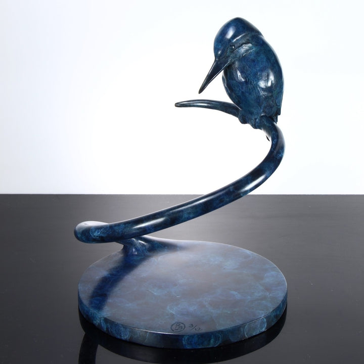 ‘Halcyon Days Maquette’ by Pat Bull, a limited-edition contemporary bronze wildlife sculpture depicting a kingfisher perched on a sweeping spiral bronze support, its head lowered and pointed beak angled towards the circular base below. The bird features finely detailed wing feathers and a smooth, rounded body finished in deep blue, navy and turquoise patina. The curved bronze stem and circular base share a mottled blue-green finish, creating a compact, elegant sculpture inspired by British wildlife.