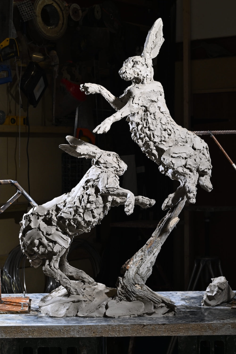 ‘Boxing Hares’ by Hamish Mackie, a limited-edition bronze wildlife sculpture depicting two hares leaping and boxing in mid-air during their characteristic springtime courtship behaviour. The dynamic composition captures their extended limbs, twisting bodies and expressive movement, with richly textured surfaces that convey the energy of the original hand-modelled clay. Photograph shows the original clay sculpture prior to bronze casting.