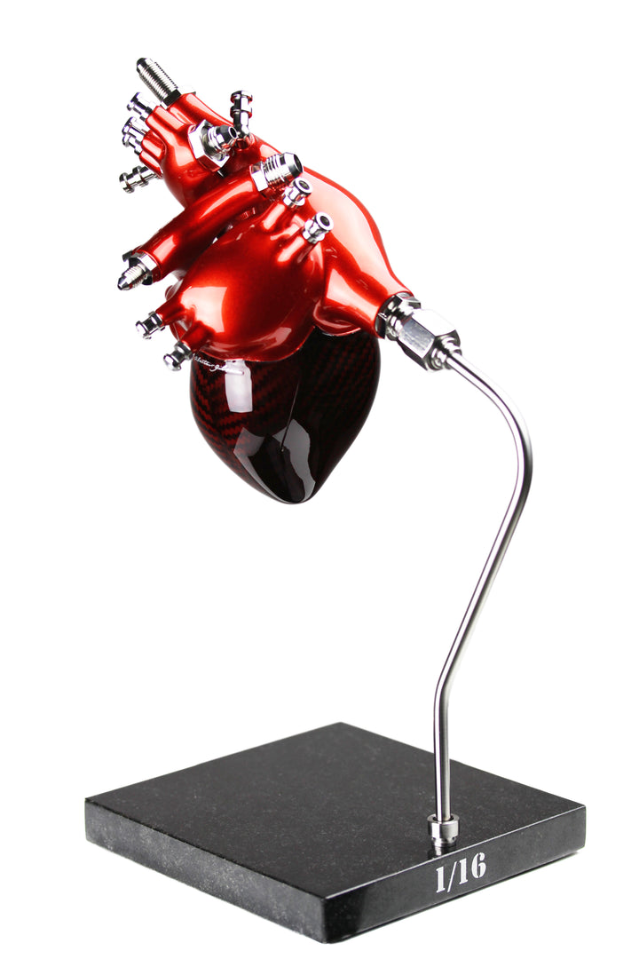 A vivid heart sculpture by Alastair Gibson, crafted from red-tinted 2x2 twill carbon fibre and finished with 3D-printed ABS atriums. Featuring titanium fuel and hydraulic fittings from Grand Prix cars, it fuses organic form with motorsport engineering. Finished in deep racing red with a UV-resistant gloss, it’s desk-mounted on a polished granite base with a stainless steel hydraulic support—blending precision with striking visual impact.