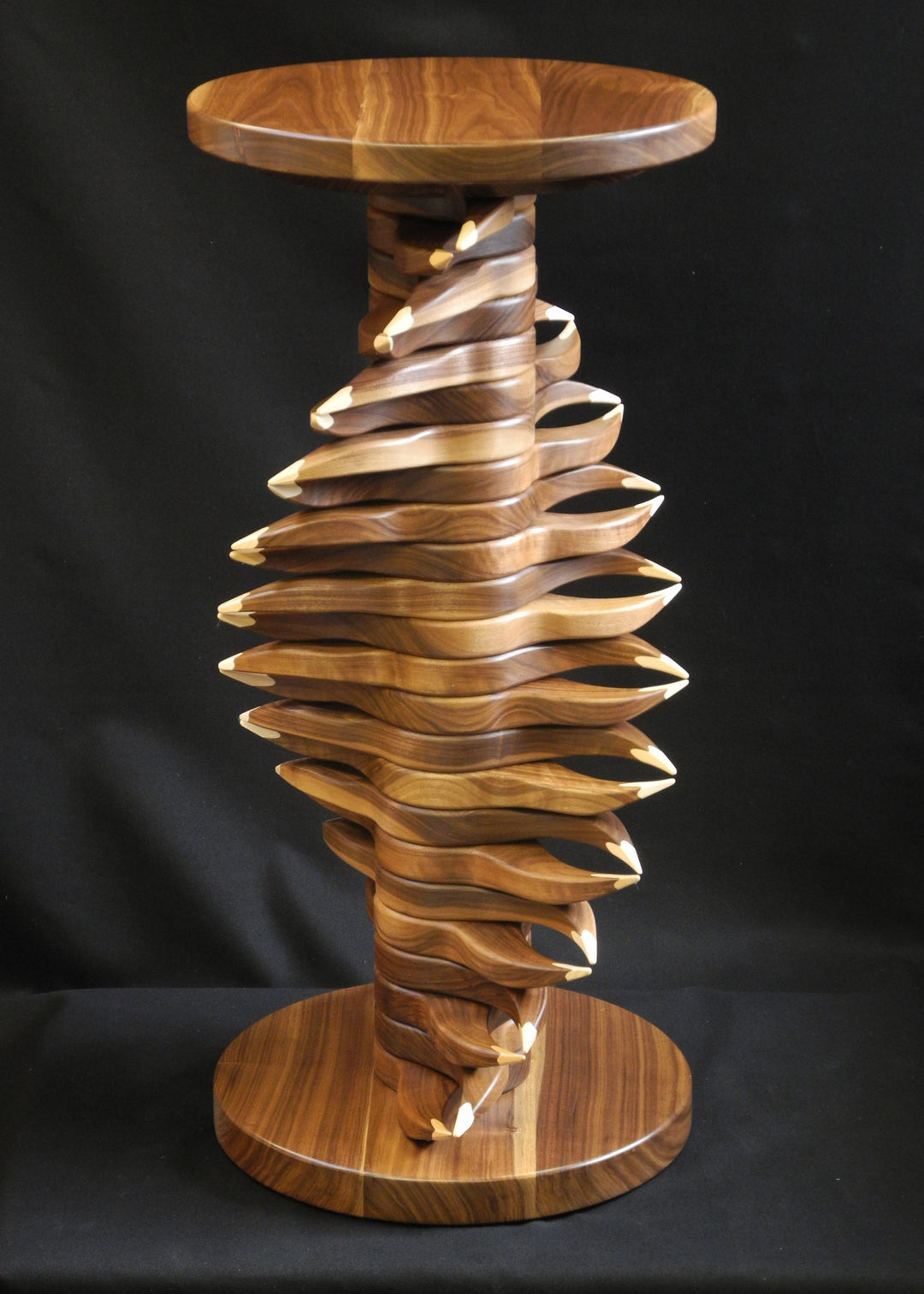 Sculptural helix table handcrafted in black walnut and maple, its spiralling layers twisting upward in a rhythmic, organic flow with pointed pale maple accents creating striking contrast against the dark walnut grain.