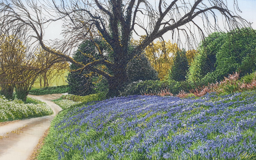 Textile artwork depicting a bluebell-covered landscape with a large oak tree and winding path, created with freehand machine embroidery on painted silk.