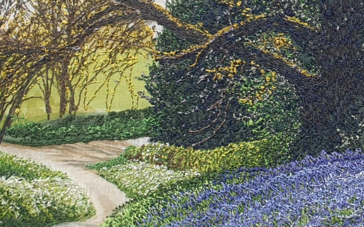 Textile artwork depicting a bluebell-covered landscape with a large oak tree and winding path, created with freehand machine embroidery on painted silk.