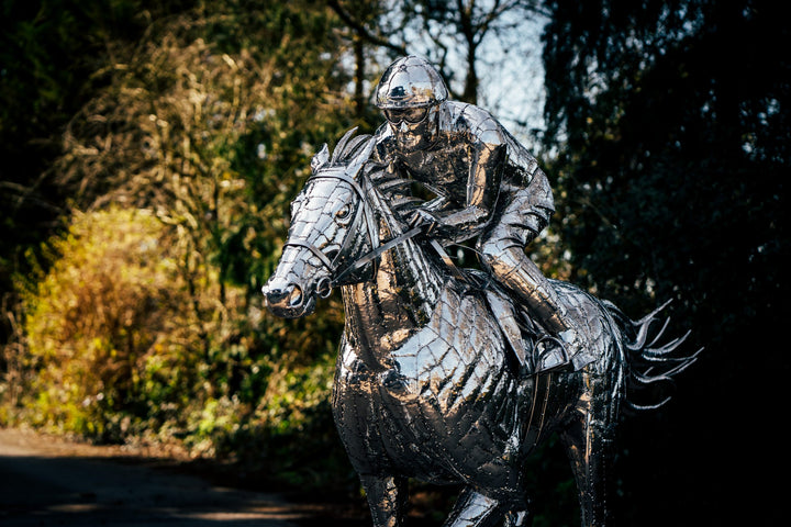 ‘Racehorse & Jockey - A Dynamic Force’ by Michael Turner, a unique, one-of-one stainless steel equestrian sculpture depicting a powerful thoroughbred racehorse galloping at full speed with its jockey leaning forward in a racing position. Handcrafted from hundreds of individually shaped and welded marine-grade stainless steel pieces, the sculpture features a polished silver finish, detailed muscular anatomy, flowing mane and tail, and a helmeted jockey holding the reins. Accompanied by a small running bird, 