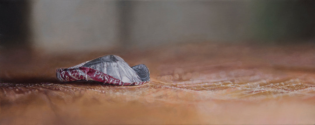 Simon Taylor, How The End Always Is, oil on canvas, 17 x 41cm – photorealist painting of a crumpled red and silver bottle cap resting on a warm brown wooden surface with shallow depth of field and soft blurred background.