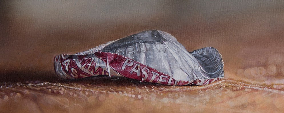 Simon Taylor, How The End Always Is, oil on canvas, 17 x 41cm – photorealist painting of a crumpled red and silver bottle cap resting on a warm brown wooden surface with shallow depth of field and soft blurred background.