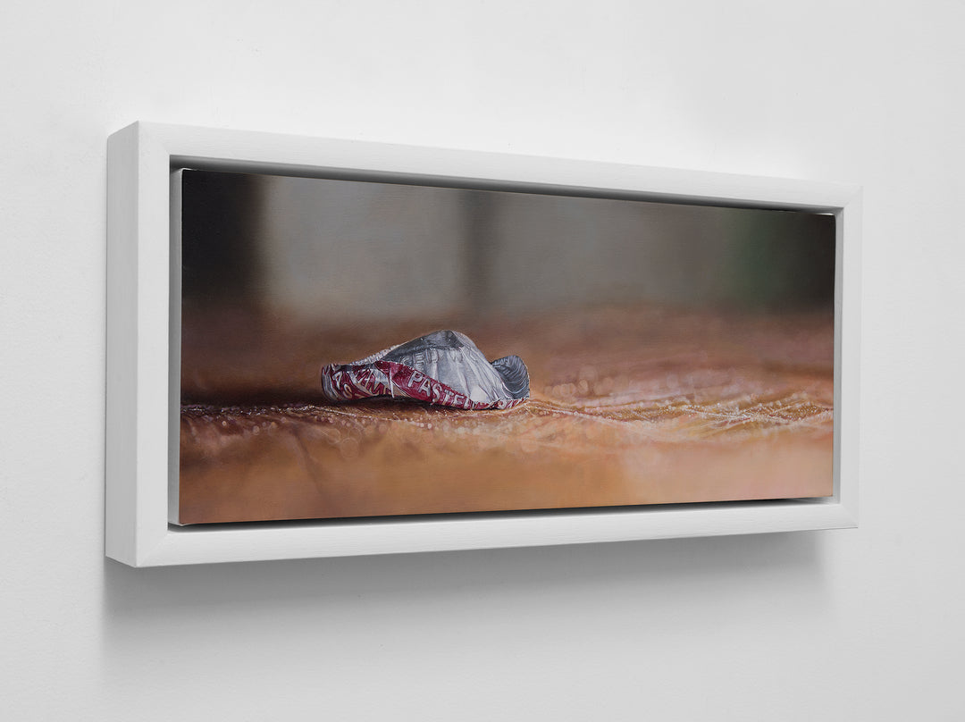 Simon Taylor, How The End Always Is, oil on canvas, 17 x 41cm – photorealist painting of a crumpled red and silver bottle cap resting on a warm brown wooden surface with shallow depth of field and soft blurred background.