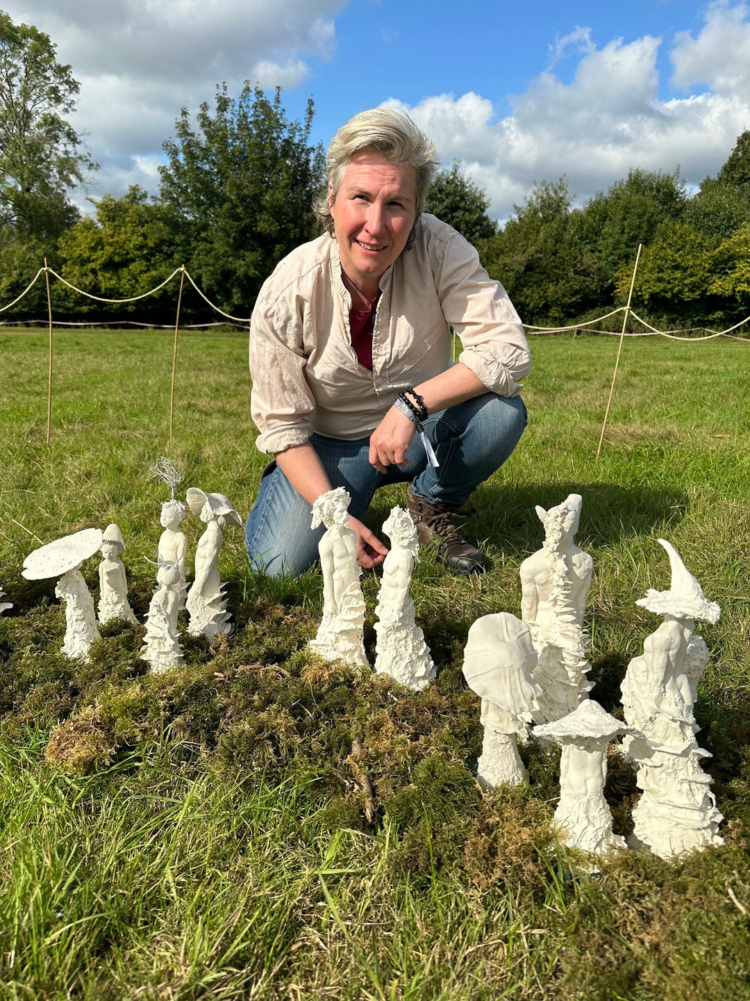 Eve Shepherd Children of Nature sculptural installation featuring around 100 individual porcelain hybrid figures combining human, animal, plant and fungal forms, arranged in a large illuminated fairy ring surrounded by natural moss.