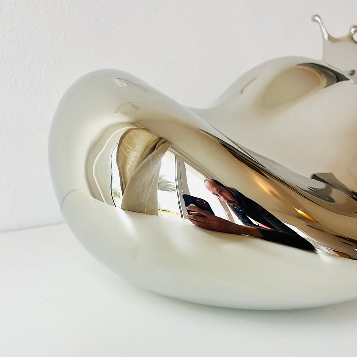 Polished stainless steel sculpture by Yoni Alter capturing the elegant moment of a liquid droplet mid-bounce. The reflective form twists fluidly to the left, with raised crown-like peaks suggesting impact and motion. A sculptural meditation on impermanence and form, grounded by a hidden counterweight for stability.