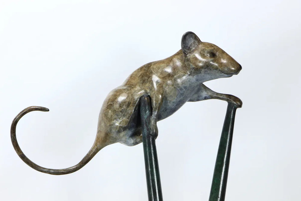 Bronze sculpture of a curious mouse perched high atop two crossed stilts, tail arched playfully behind, poised in a moment of bold exploration and balance.