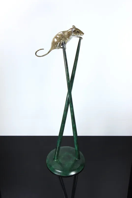 Bronze sculpture of a curious mouse perched high atop two crossed stilts, tail arched playfully behind, poised in a moment of bold exploration and balance.