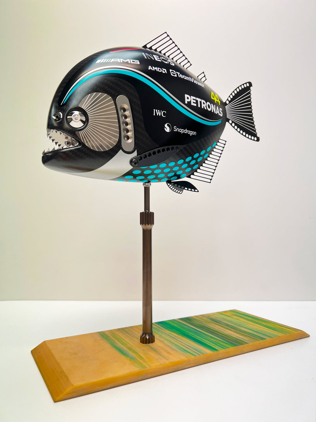 Close-up views of Predator in Motion – a sculptural fusion of engineering and marine form by Alastair Gibson. The body is formed from layered carbon fibre with a matte black finish and turquoise vinyl livery inspired by Lewis Hamilton’s 2023 Mercedes AMG Formula One car. Sponsor graphics include Petronas, Ineos, AMD, and TeamViewer. Satin black stainless steel fins and titanium teeth reflect precision F1 detailing. Polished titanium eyes are inset with a pink diamond-effect crystal. Mounted on a torsion bar