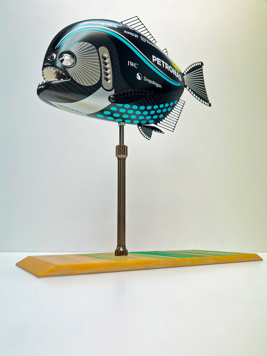 Close-up views of Predator in Motion – a sculptural fusion of engineering and marine form by Alastair Gibson. The body is formed from layered carbon fibre with a matte black finish and turquoise vinyl livery inspired by Lewis Hamilton’s 2023 Mercedes AMG Formula One car. Sponsor graphics include Petronas, Ineos, AMD, and TeamViewer. Satin black stainless steel fins and titanium teeth reflect precision F1 detailing. Polished titanium eyes are inset with a pink diamond-effect crystal. Mounted on a torsion bar