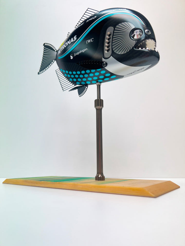 Close-up views of Predator in Motion – a sculptural fusion of engineering and marine form by Alastair Gibson. The body is formed from layered carbon fibre with a matte black finish and turquoise vinyl livery inspired by Lewis Hamilton’s 2023 Mercedes AMG Formula One car. Sponsor graphics include Petronas, Ineos, AMD, and TeamViewer. Satin black stainless steel fins and titanium teeth reflect precision F1 detailing. Polished titanium eyes are inset with a pink diamond-effect crystal. Mounted on a torsion bar