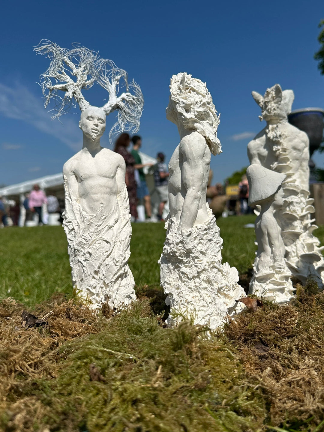 Eve Shepherd Children of Nature sculptural installation featuring around 100 individual porcelain hybrid figures combining human, animal, plant and fungal forms, arranged in a large illuminated fairy ring surrounded by natural moss.