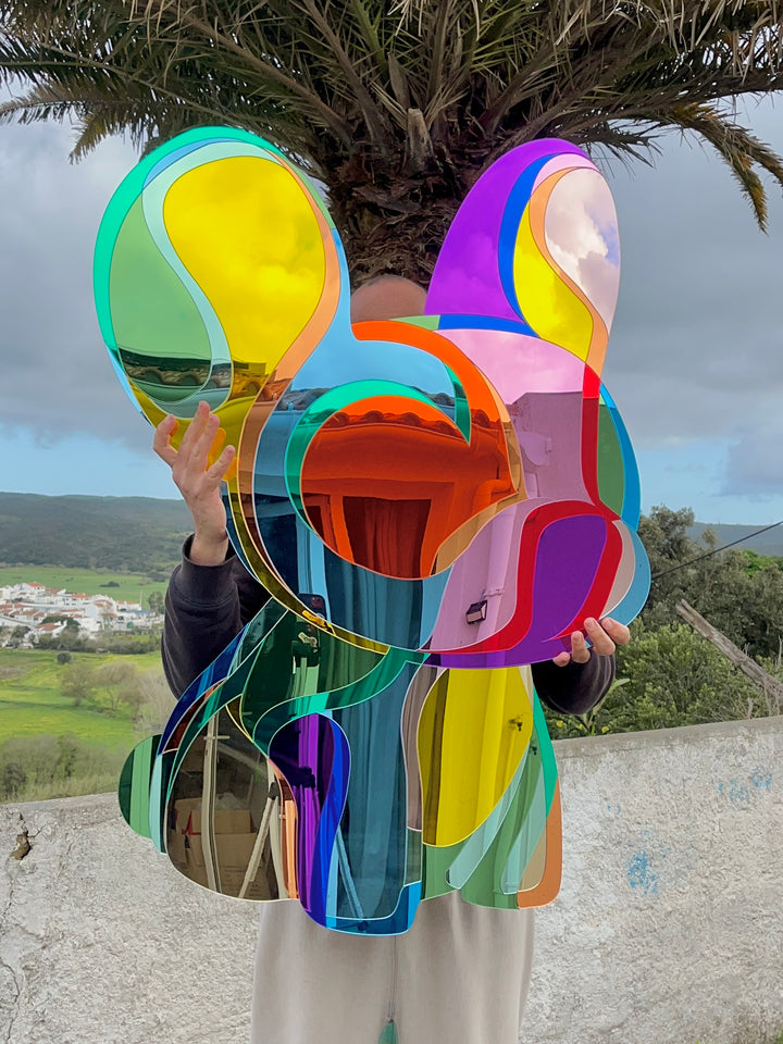 Vibrant, multi-coloured wall sculpture by Yoni Alter in the shape of a stylised French Bulldog, crafted from layered acrylic mirrors with bold, fluid contours and a high-gloss finish. The reflective surfaces create playful distortions of light and environment, merging pop art energy with contemporary design.