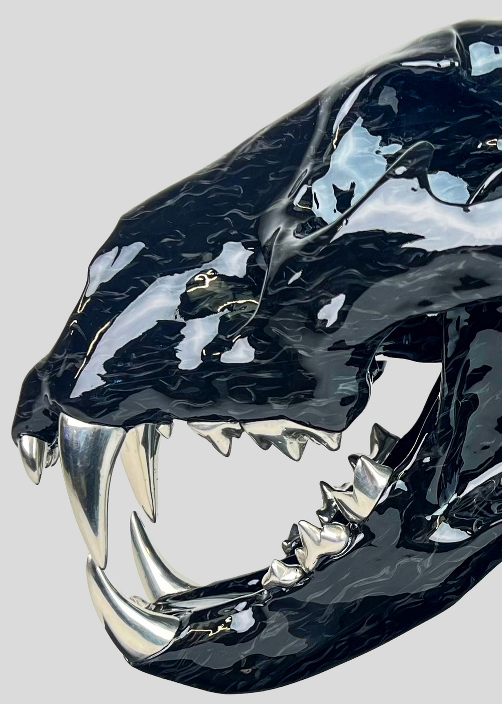 A striking, polished carbon fibre lion skull sculpture by Alastair Gibson, crafted with Mokume-style carbon layup for a swirling, chaotic texture. The jaw is fitted with gleaming bismuth alloy teeth. Mounted on a genuine F1 gearbox selector barrel atop a granite base, the work merges natural form with elite motorsport engineering.