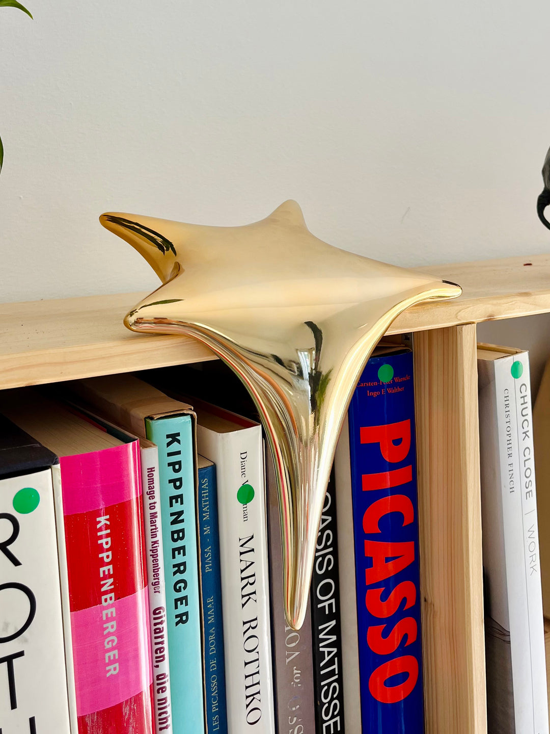 Polished gold-toned stainless steel sculpture in the form of a stylised shooting star, with a fluid, elongated spike melting over the edge of a white plinth or shelf.