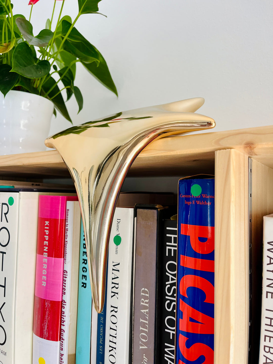 Polished gold-toned stainless steel sculpture in the form of a stylised shooting star, with a fluid, elongated spike melting over the edge of a white plinth or shelf.