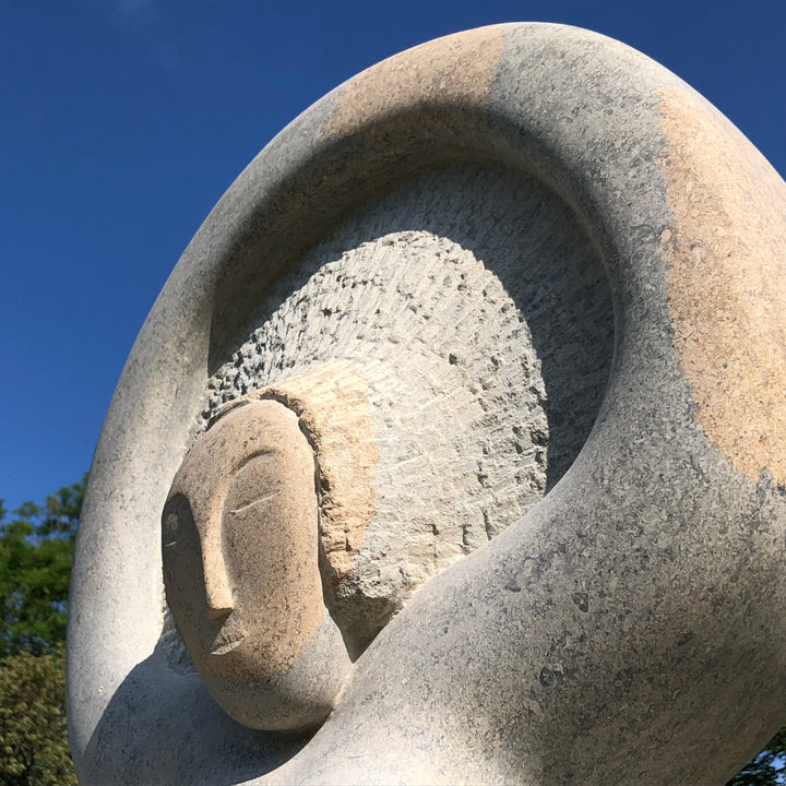 ‘Sunrise’ by Nicolas Moreton MRSS, a unique contemporary figurative stone sculpture carved from Ancaster Weatherbed Limestone, depicting a stylised seated female figure with crossed legs and raised arms forming a circular halo-like shape above her head. The figure features a delicately carved face, textured hair and smooth, rounded body, emerging from a large rectangular limestone block with a rough natural surface and flowing carved folds. Finished in warm cream, pale beige and natural limestone tones, the