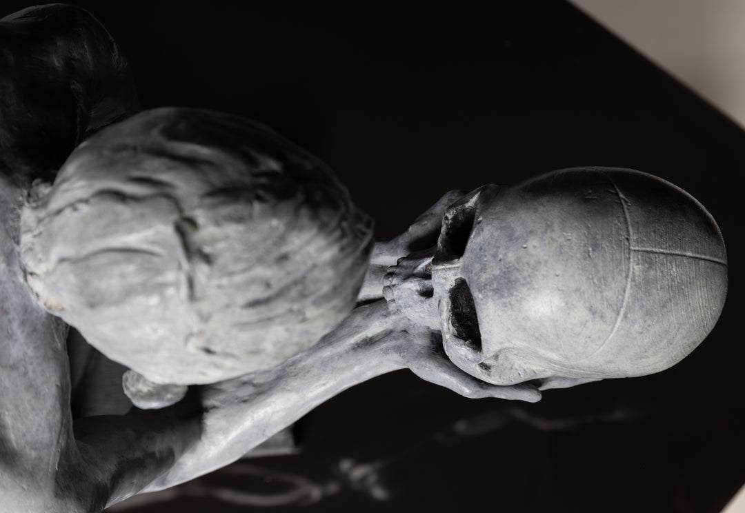 Teresa Wells’ The Prophecy (2024), limited edition bronze sculpture depicting a crouched, nude figure balanced atop stacked books, holding a human skull in both hands and gazing intently into its hollow eyes. Finished in a pale grey patina with darker shading to emphasise musculature and contours, the piece evokes themes of mortality, knowledge, and forewarning. At 30cm × 25cm × 49cm and 23.4kg, it combines fine anatomical detail, symbolic elements, and a contemporary reinterpretation of classical imagery.