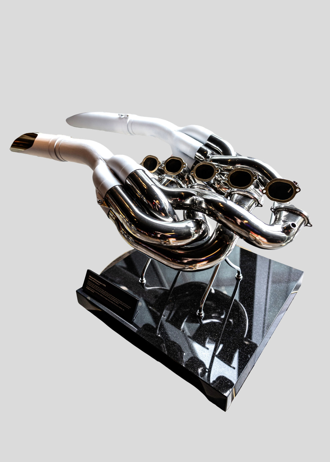 Highly polished sculptural artwork by Mike O’Connor crafted from the authentic race-used exhaust system of Michael Schumacher’s 1995 Benetton B195 Formula One car. The piece features flowing Inconel and stainless-steel pipes with mirror-finished chrome surfaces and 24-karat gold interior detailing, mounted on a sleek stand. A striking one-of-one collector’s piece 