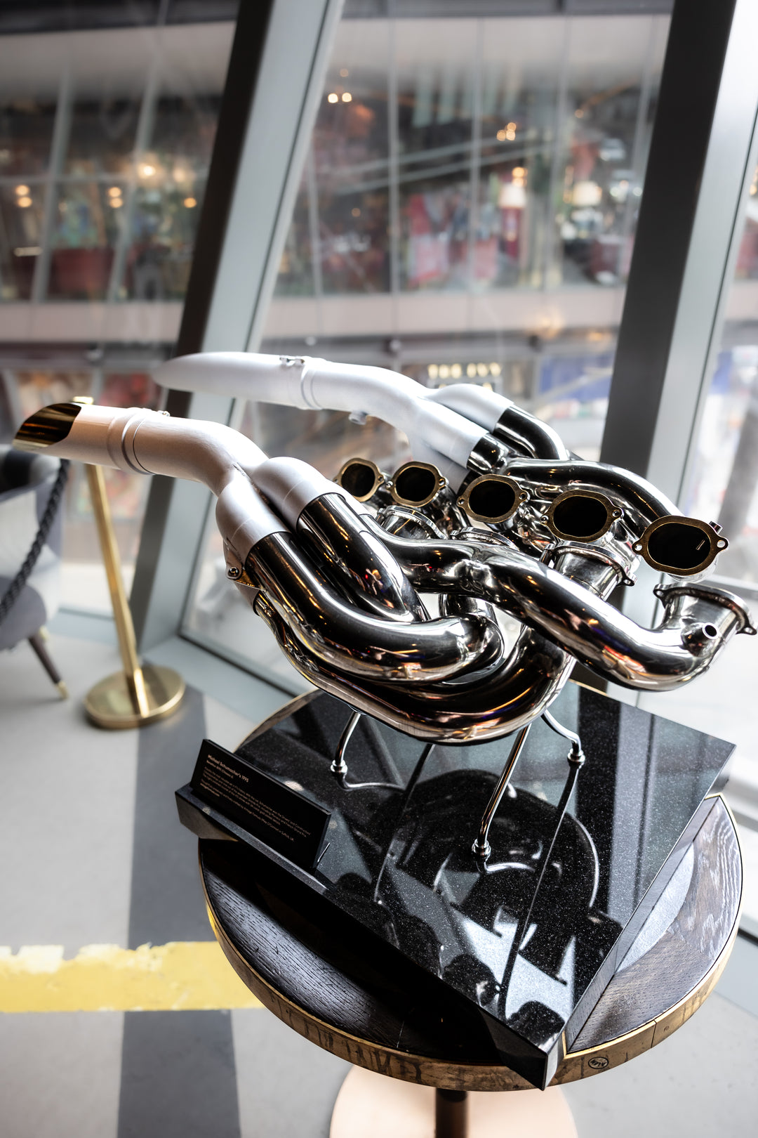 Highly polished sculptural artwork by Mike O’Connor crafted from the authentic race-used exhaust system of Michael Schumacher’s 1995 Benetton B195 Formula One car. The piece features flowing Inconel and stainless-steel pipes with mirror-finished chrome surfaces and 24-karat gold interior detailing, mounted on a sleek stand. A striking one-of-one collector’s piece 