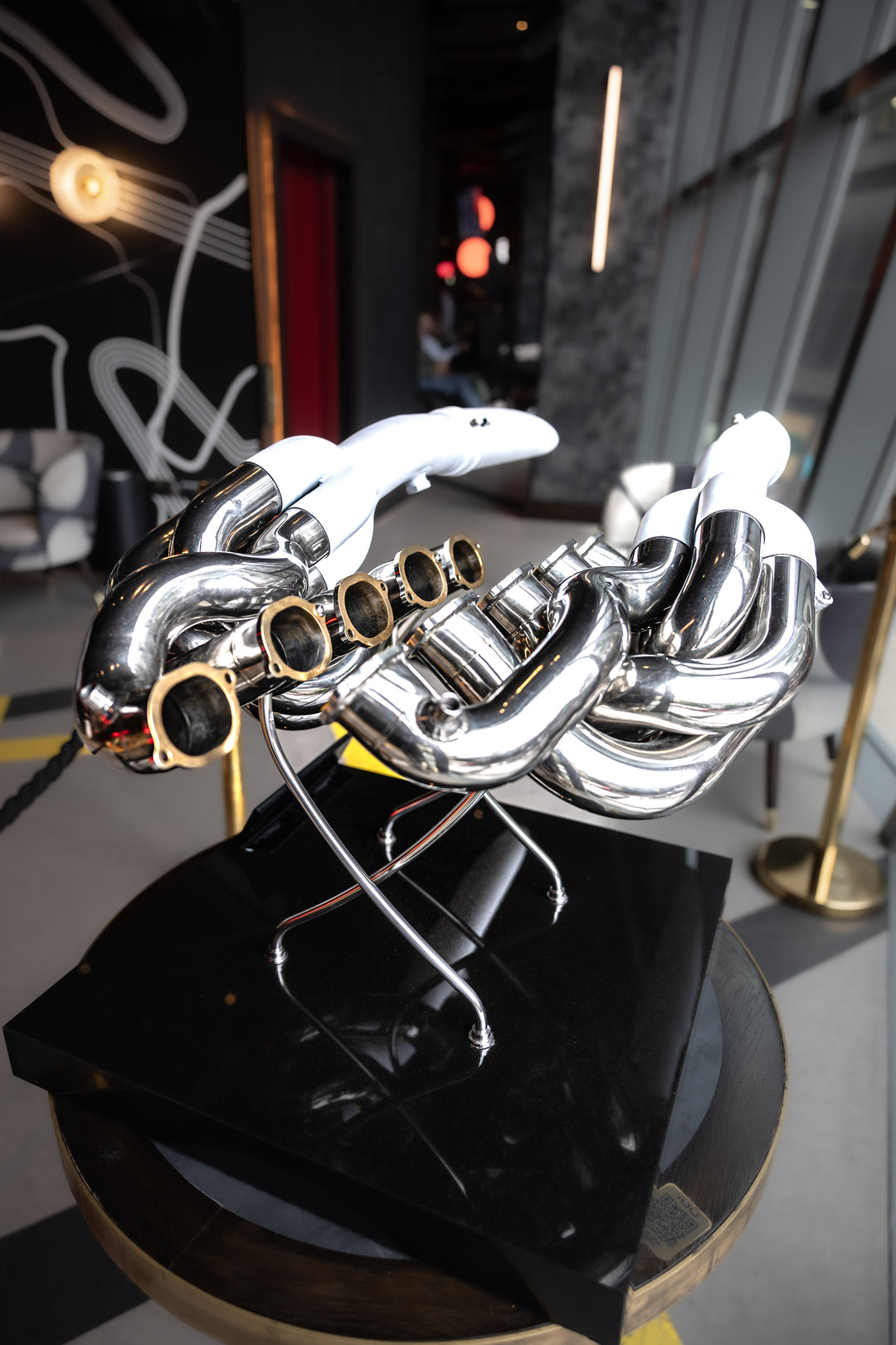 Highly polished sculptural artwork by Mike O’Connor crafted from the authentic race-used exhaust system of Michael Schumacher’s 1995 Benetton B195 Formula One car. The piece features flowing Inconel and stainless-steel pipes with mirror-finished chrome surfaces and 24-karat gold interior detailing, mounted on a sleek stand. A striking one-of-one collector’s piece 