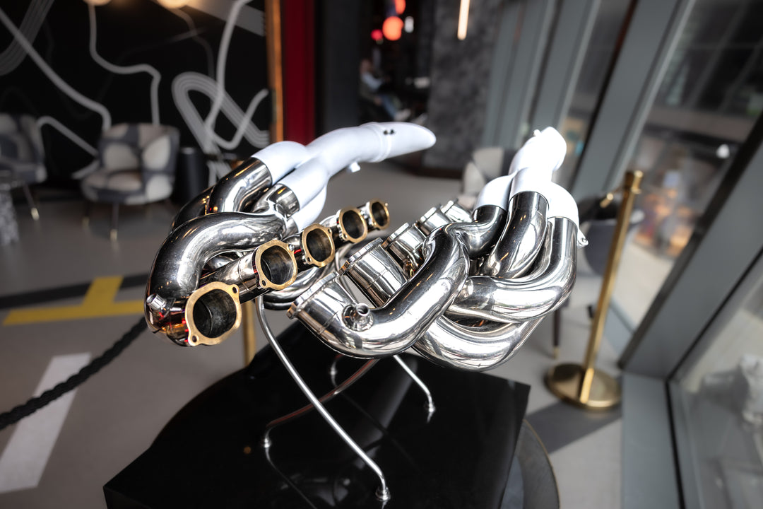 Highly polished sculptural artwork by Mike O’Connor crafted from the authentic race-used exhaust system of Michael Schumacher’s 1995 Benetton B195 Formula One car. The piece features flowing Inconel and stainless-steel pipes with mirror-finished chrome surfaces and 24-karat gold interior detailing, mounted on a sleek stand. A striking one-of-one collector’s piece 