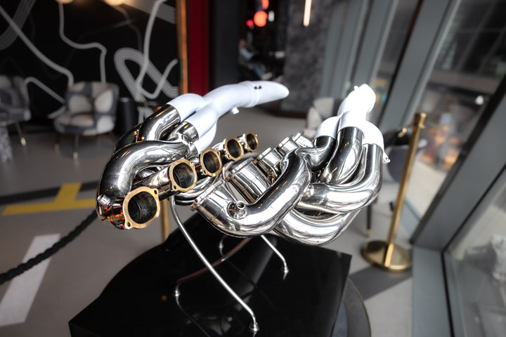 Highly polished sculptural artwork by Mike O’Connor crafted from the authentic race-used exhaust system of Michael Schumacher’s 1995 Benetton B195 Formula One car. The piece features flowing Inconel and stainless-steel pipes with mirror-finished chrome surfaces and 24-karat gold interior detailing, mounted on a sleek stand. A striking one-of-one collector’s piece 
