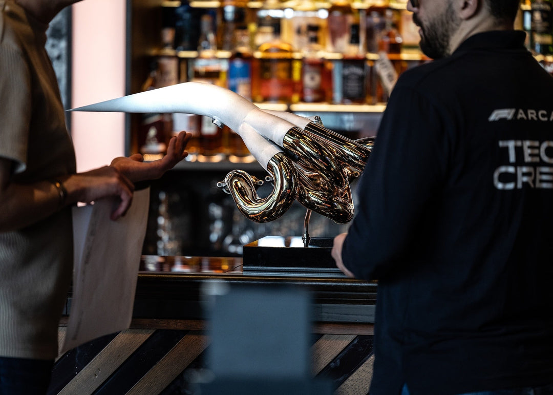 One-of-one sculpture by Mike O’Connor created from the authentic, race-used exhaust system of the 2001 Jordan EJ11 Formula One car. The polished Inconel structure gleams with precision and craftsmanship, while the internal surfaces are plated in 24-karat gold—a tribute to the heat and resonance of the V10 era. Mounted on a sleek black plinth